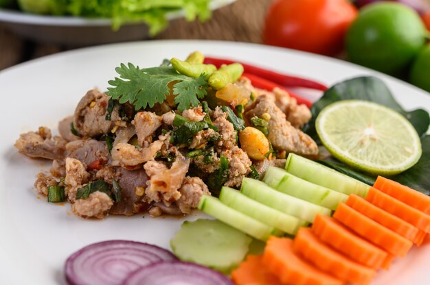 Ensalada de carne de cerdo picada picante en un plato blanco sobre mesa de madera.