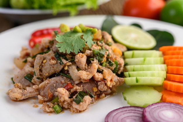 Ensalada de carne de cerdo picada picante en un plato blanco sobre mesa de madera.