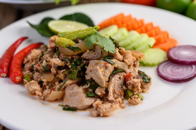 Ensalada de carne de cerdo picada picante en un plato blanco sobre mesa de madera.