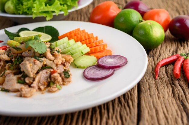 Ensalada de carne de cerdo picada picante en un plato blanco sobre mesa de madera.