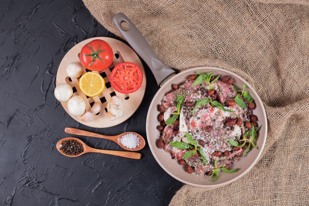 Ensalada de carne cruda con menta fresca en sartén y plato de verduras frescas.