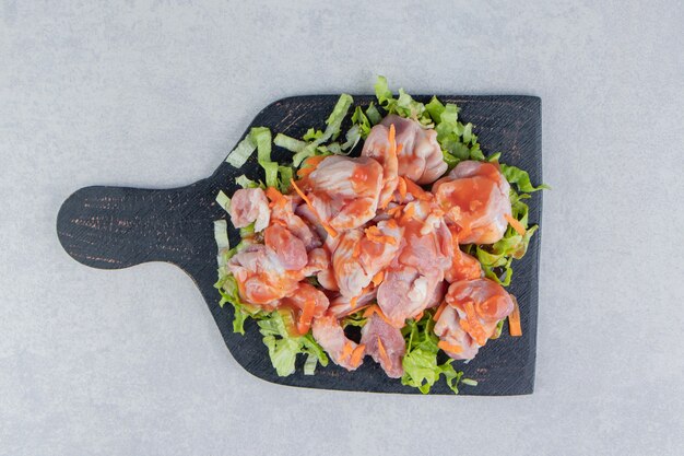 Ensalada y carne cruda en el tablero, sobre la superficie blanca