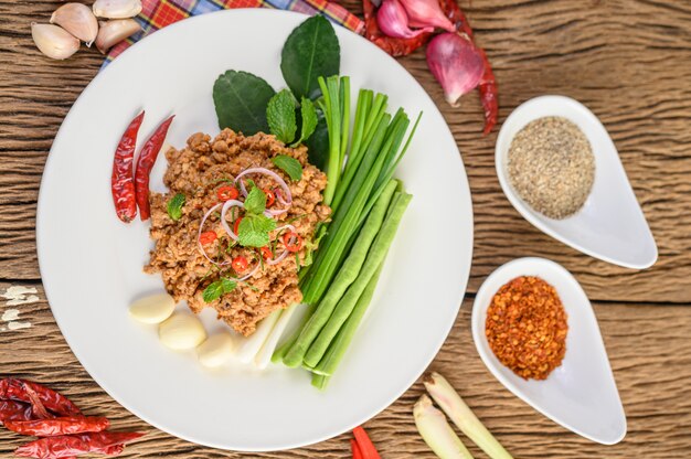 Ensalada de carne picada de cerdo picada en un plato blanco con cebolla roja, hierba de limón, ajo, judías largas, hojas de lima kaffir y cebolla tierna