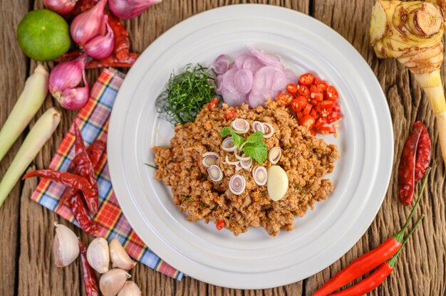 Ensalada de carne picada de cerdo picada en un plato blanco con cebolla roja, hierba de limón, ajo, judías largas, hojas de lima kaffir y cebolla tierna