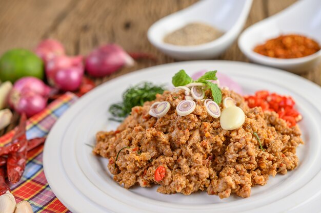 Ensalada de carne picada de cerdo picada en un plato blanco con cebolla roja, hierba de limón, ajo, judías largas, hojas de lima kaffir y cebolla tierna