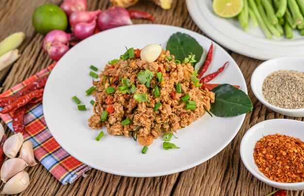 Ensalada de carne picada de cerdo picada en un plato blanco con cebolla roja, hierba de limón, ajo, judías largas, hojas de lima kaffir y cebolla tierna