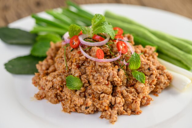 Ensalada de carne picada de cerdo picada en un plato blanco con lentejas, hojas de lima kaffir y cebolletas.