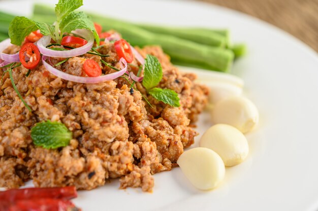 Ensalada de carne picada de cerdo picada en un plato blanco con lentejas, hojas de lima kaffir y cebolletas.