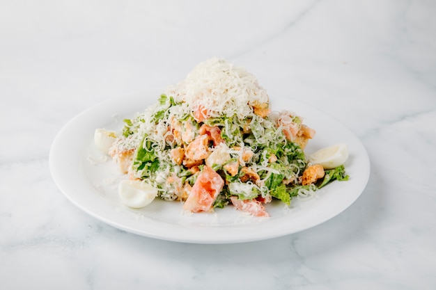 Ensalada César con ingredientes mixtos y queso picado en la parte superior en fondo blanco.