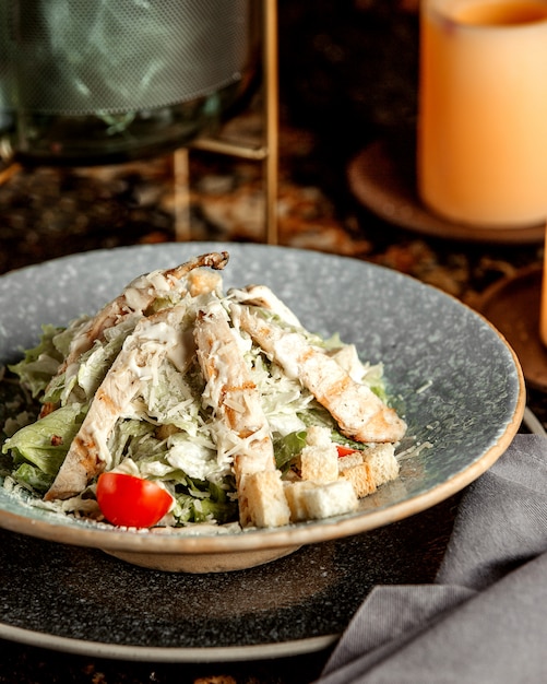 Ensalada César con pollo, lechuga, tomate, galletas y queso rallado.