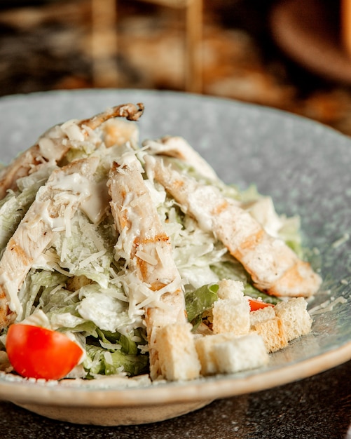 Ensalada César con pollo, lechuga, tomate, galletas y queso rallado.