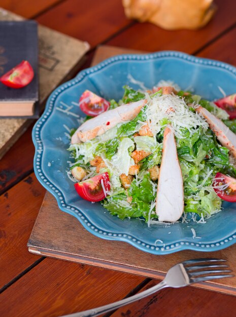 Ensalada César de pollo con queso parmesano picado, lechuga fresca y tomates, galletas en un plato azul.