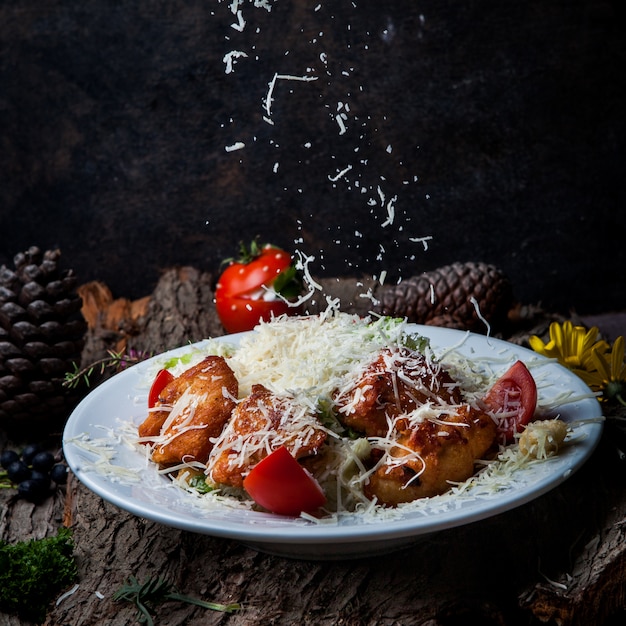 Ensalada César con pollo, tomate, lechuga, aceitunas, galletas saladas, queso parmesano en un plato blanco sobre una corteza de árbol oscuro