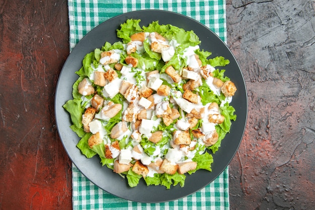 Ensalada César de vista superior en plato ovalado mantel a cuadros blanco verde sobre fondo rojo oscuro