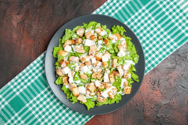 Ensalada César de vista superior en plato ovalado mantel a cuadros blanco verde sobre mesa oscura