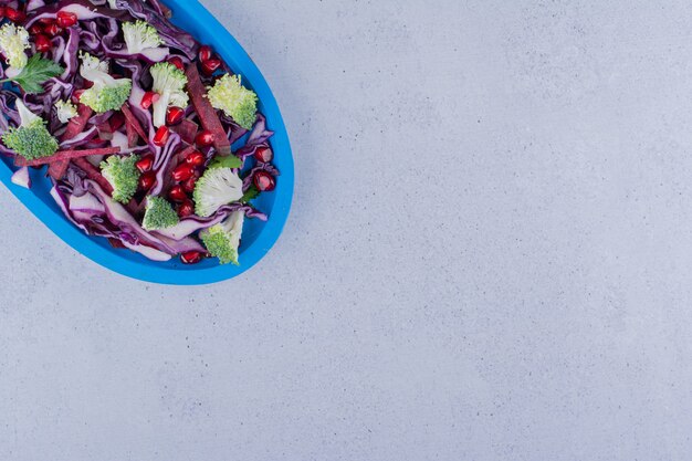 Ensalada de col lombarda picada y brócoli mezclada con arilos de granada sobre fondo de mármol. Foto de alta calidad