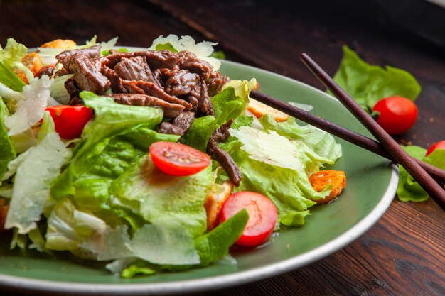 Ensalada deliciosa comida en un plato con palillos sobre un fondo de madera vista de ángulo alto