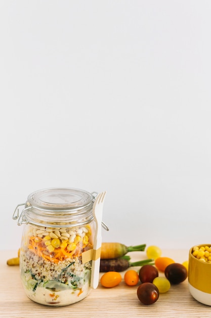 Ensalada fresca de primavera en frasco cerrado con tenedor blanco y verduras en mesa de madera