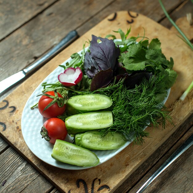 Ensalada fresca superior con pepinos, tomates y hierbas en un plato sobre madera