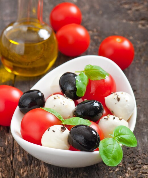 Ensalada fresca con tomates cherry, albahaca, mozzarella y aceitunas negras.