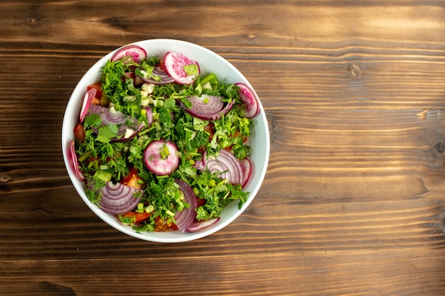 Ensalada fresca vitaminada rica en colorido con rábano cebolla roja y tomates en el interior con verduras en la parte superior en la superficie rústica de madera