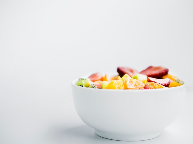 Ensalada de fruta fresca sabrosa en un tazón sobre fondo blanco