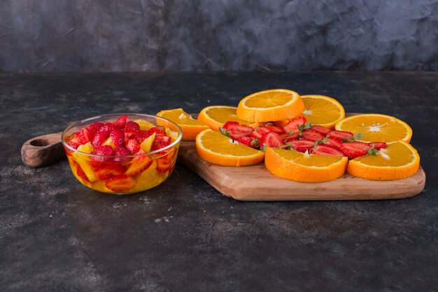 Ensalada de frutas con fresas y naranjas con tabla de frutas a un lado