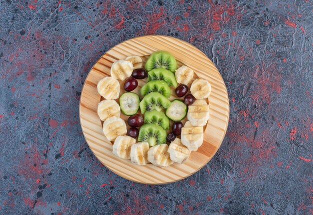 Ensalada de frutas con rodajas de plátano, kiwies y bayas en una placa de madera.