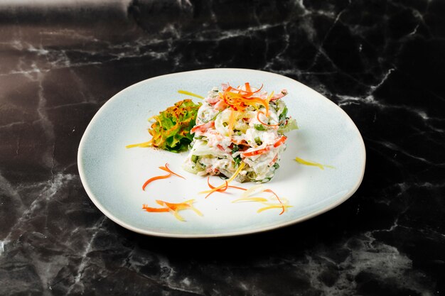 Ensalada de ingredientes mezclados dentro de un plato blanco sobre un mármol negro.