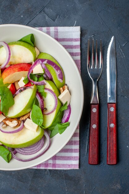 Ensalada de manzana fresca vista superior en plato redondo en cuchillo y tenedor de mantel a cuadros púrpura y blanco sobre fondo negro