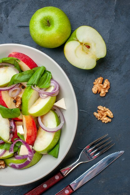 Ensalada de manzana fresca vista superior en plato redondo manzanas nuez tenedor y cuchillo en mesa oscura