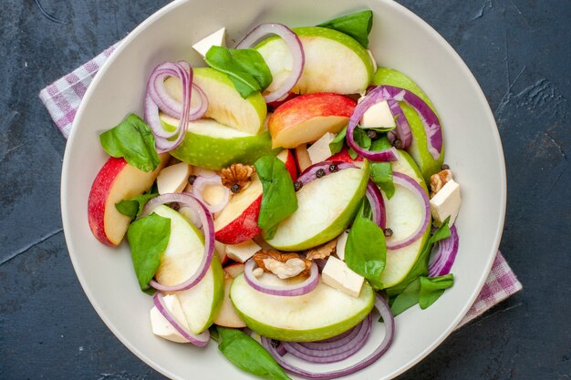 Ensalada de manzana de vista superior cercana en tazón de fuente servilleta a cuadros púrpura y blanco sobre mesa oscura