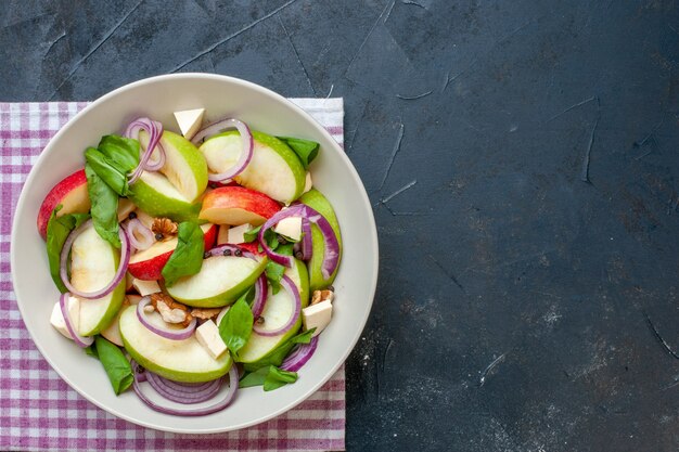 Ensalada de manzana vista superior en tazón de fuente servilleta a cuadros púrpura y blanco sobre mesa oscura con lugar de copia