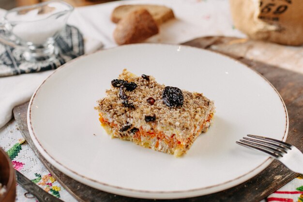 Ensalada mayonesa diseñada verduras con ciruela seca negra dentro de un plato blanco junto con panes de pan