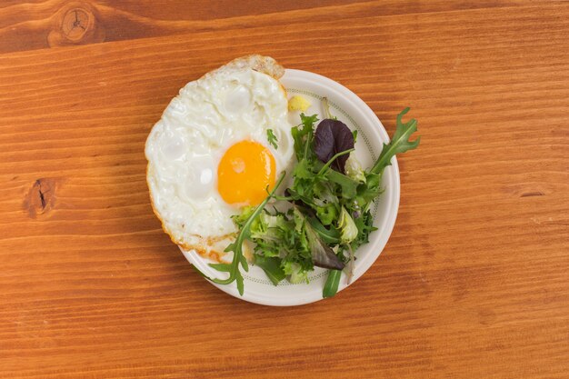 Ensalada y medio huevo frito en un plato sobre la mesa de madera