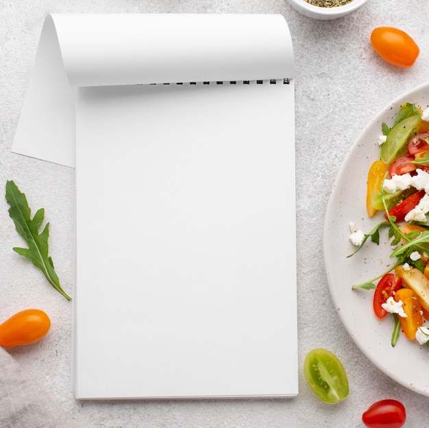 Ensalada de mezcla de tomate vista superior con queso feta y bloc de notas en blanco