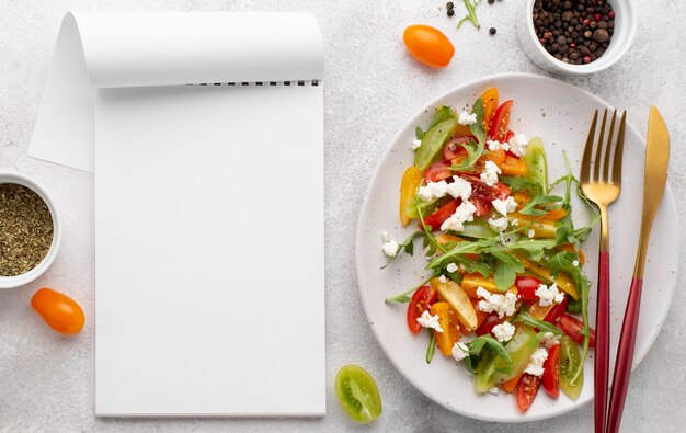 Ensalada de mezcla de tomate vista superior con queso feta y cuaderno en blanco