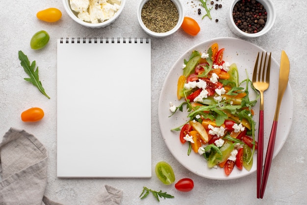 Ensalada de mezcla de tomate vista superior con queso feta, rúcula y cuaderno en blanco