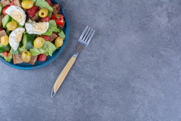 Ensalada mixta de huevos, pepino, tomate, aceitunas y lechuga sobre superficie de mármol