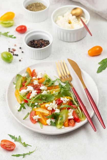 Ensalada mixta de tomate de alto ángulo con queso feta, rúcula y cubiertos