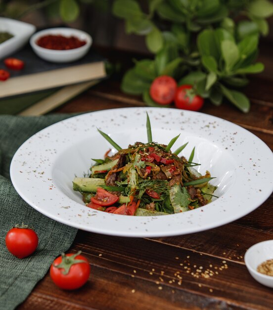 Ensalada mixta de verduras con hierbas dentro de un plato blanco sobre una mesa de madera