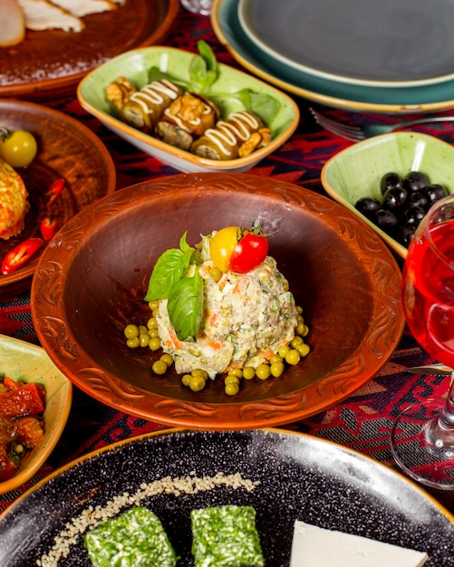 Ensalada Olivier decorada con guisantes, tomate y albahaca