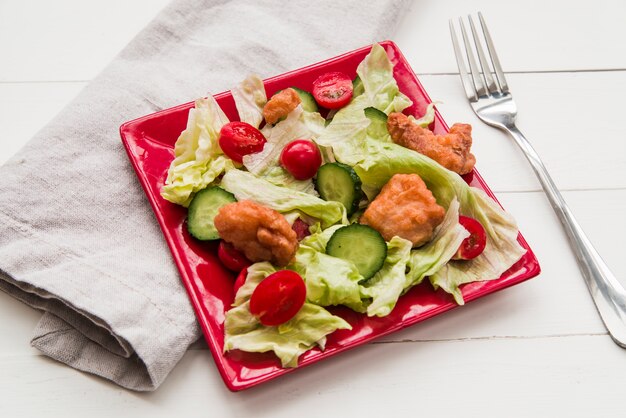 Ensalada de palomitas de maíz crujiente decorada con verduras en un plato rojo con servilleta y tenedor