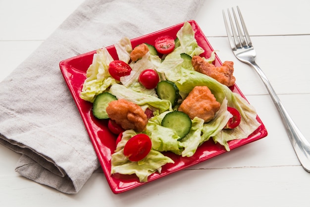 Ensalada de palomitas de maíz crujiente decorada con verduras en un plato rojo con servilleta y tenedor