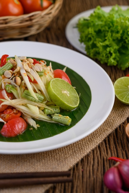 Ensalada de papaya (Som tum Thai) en un plato blanco sobre una mesa de madera.