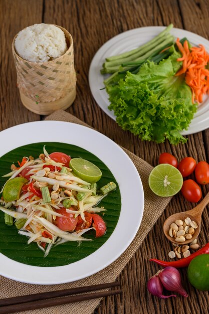 Ensalada de papaya (Som tum Thai) en un plato blanco sobre una mesa de madera.