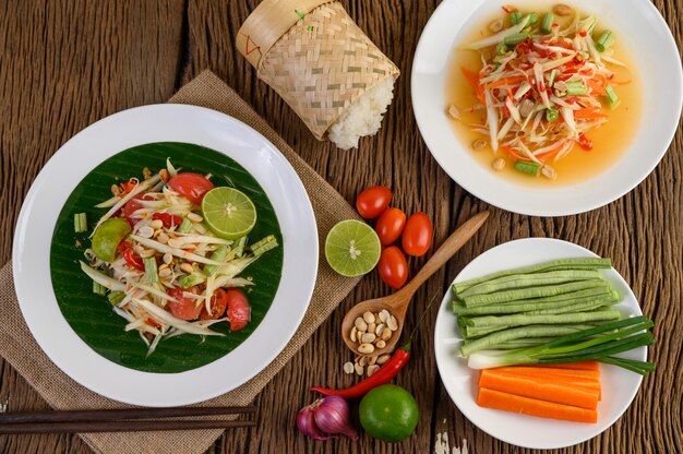 Ensalada de papaya (Som tum Thai) en un plato blanco sobre una mesa de madera.