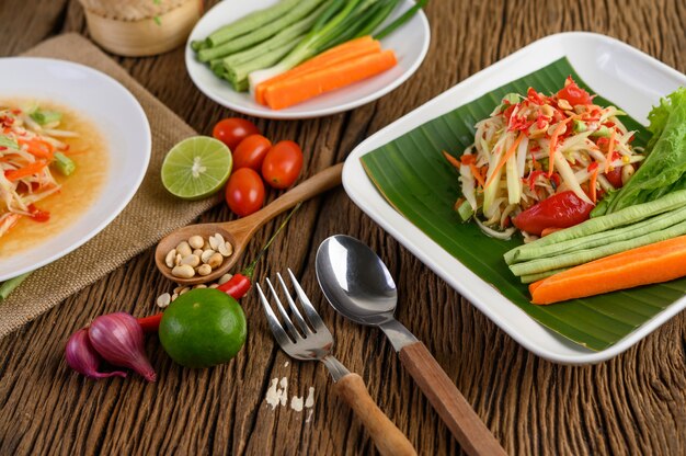 Ensalada de papaya (Som tum Thai) en un plato blanco sobre una mesa de madera.