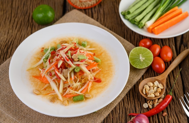 Ensalada de papaya (Som tum Thai) en un plato blanco sobre una mesa de madera.