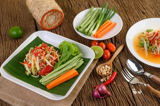 Ensalada de papaya (Som tum Thai) en un plato blanco sobre una mesa de madera.